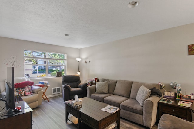 living room with visible vents, baseboards, a textured ceiling, and wood finished floors
