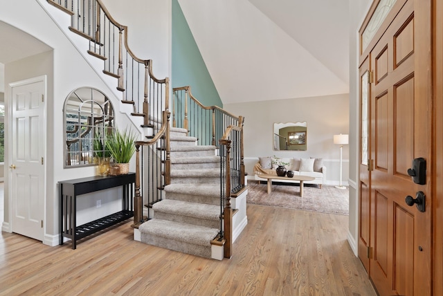 foyer with baseboards, stairs, wood finished floors, and high vaulted ceiling