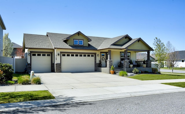 craftsman-style home featuring fence, stone siding, a garage, covered porch, and driveway