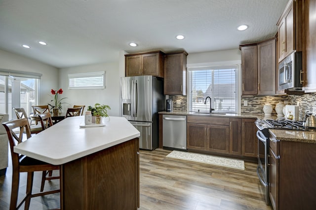 kitchen with decorative backsplash, a kitchen bar, appliances with stainless steel finishes, light wood-type flooring, and a sink