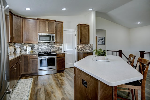 kitchen with wood finished floors, appliances with stainless steel finishes, lofted ceiling, and tasteful backsplash