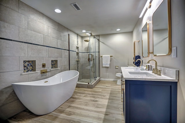 bathroom with visible vents, a stall shower, wood finished floors, a sink, and a soaking tub