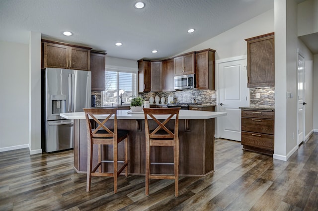 kitchen with dark brown cabinetry, a center island, stainless steel appliances, tasteful backsplash, and dark wood-style floors
