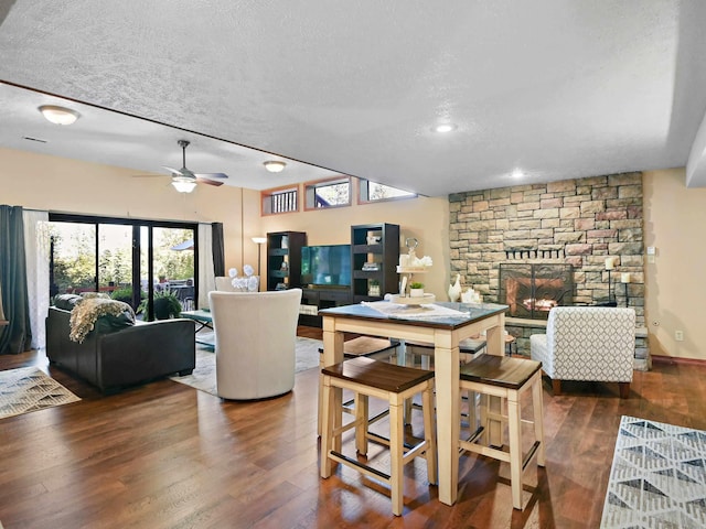 dining room with ceiling fan, a stone fireplace, a textured ceiling, and wood finished floors