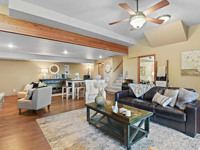 living area featuring ceiling fan, stairs, baseboards, wood finished floors, and beamed ceiling