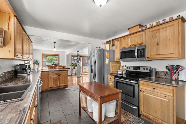 kitchen with dark countertops, appliances with stainless steel finishes, a sink, a peninsula, and dark tile patterned floors