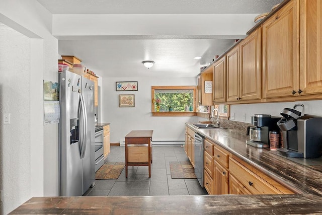 kitchen featuring appliances with stainless steel finishes, dark countertops, a sink, baseboards, and tile patterned floors