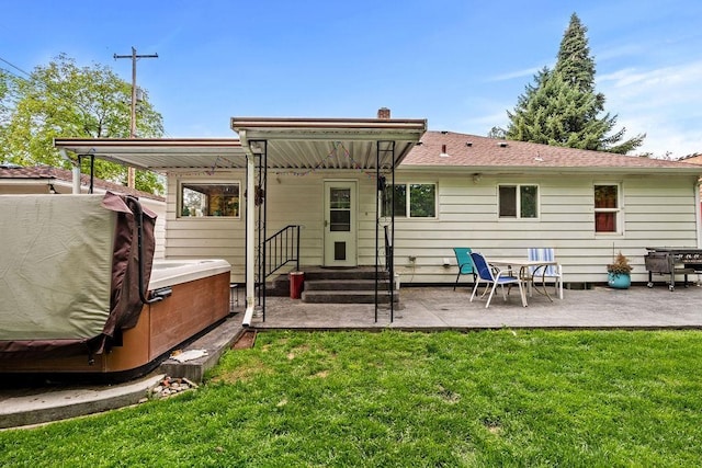rear view of property featuring a chimney, a patio area, entry steps, a lawn, and a hot tub