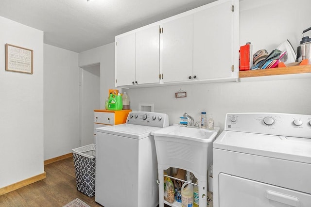 washroom featuring dark wood-style flooring, cabinet space, a sink, baseboards, and washer and clothes dryer