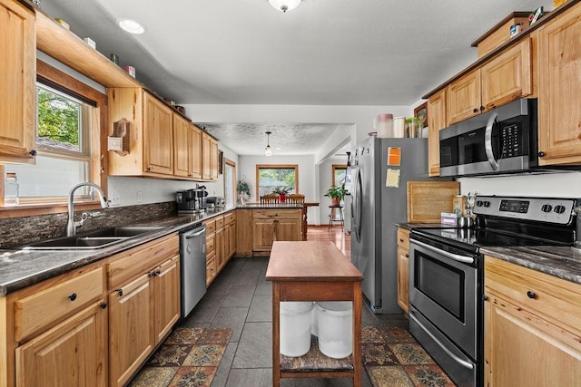 kitchen with a peninsula, dark countertops, dark tile patterned flooring, a sink, and appliances with stainless steel finishes