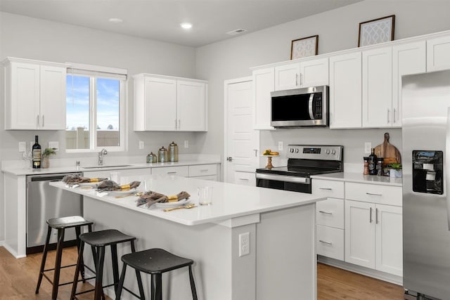 kitchen with appliances with stainless steel finishes, a breakfast bar, light wood-type flooring, and white cabinetry