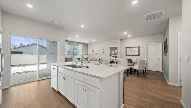 kitchen with a sink, white dishwasher, wood finished floors, and visible vents