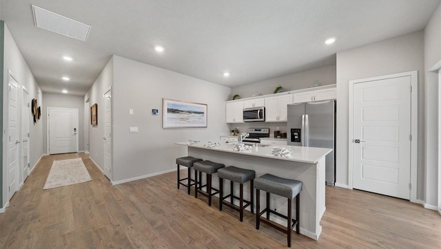 kitchen with a breakfast bar, an island with sink, stainless steel appliances, light wood-type flooring, and visible vents