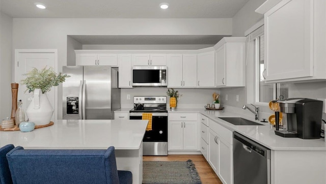 kitchen with white cabinets, a sink, light wood-style floors, light countertops, and stainless steel appliances