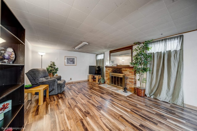 living room with a brick fireplace, baseboards, and wood finished floors