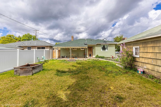 rear view of house with a garden, fence, a chimney, a patio area, and a yard