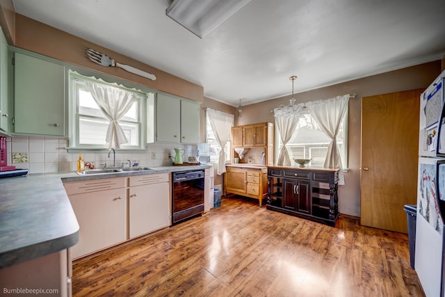 kitchen featuring decorative backsplash, pendant lighting, light wood-type flooring, a sink, and dishwasher