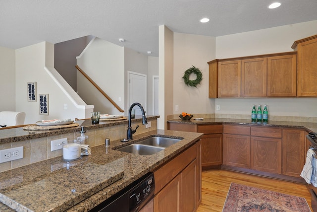 kitchen featuring brown cabinets, a sink, light wood finished floors, dark stone countertops, and recessed lighting