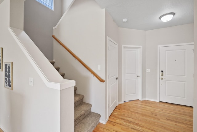 entrance foyer featuring light wood-style floors, baseboards, and stairway