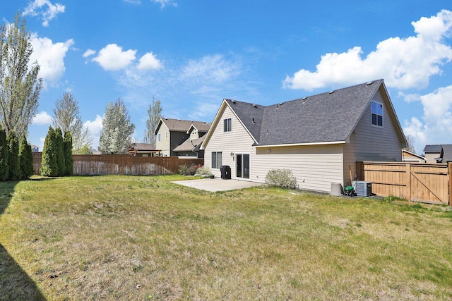 rear view of house with a shingled roof, a fenced backyard, central air condition unit, a patio, and a lawn