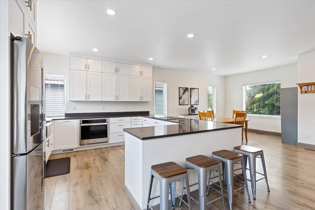 kitchen with dark countertops, light wood-style floors, a breakfast bar area, stainless steel appliances, and white cabinetry