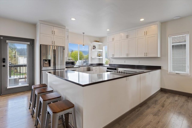 kitchen featuring a peninsula, wood finished floors, recessed lighting, white cabinets, and stainless steel appliances