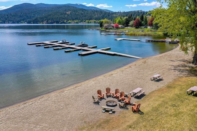 water view with a boat dock, a view of trees, a mountain view, and an outdoor fire pit