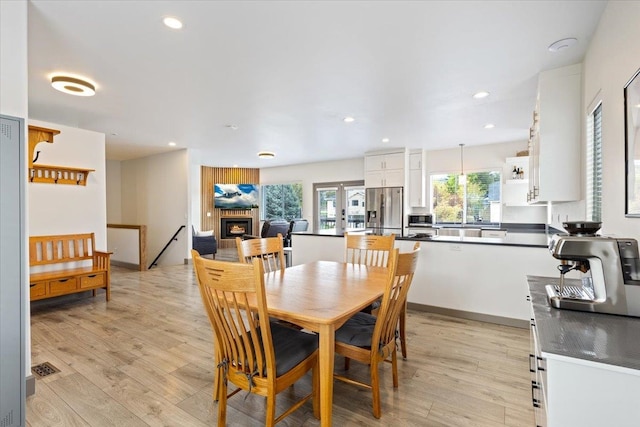 dining area featuring light wood-type flooring, recessed lighting, and a warm lit fireplace
