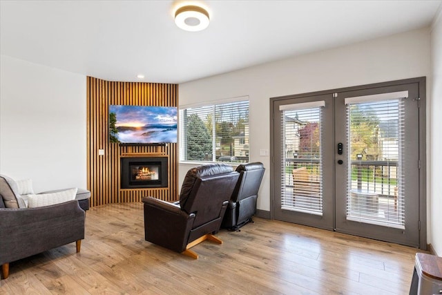 living area featuring french doors, light wood-style flooring, and a glass covered fireplace