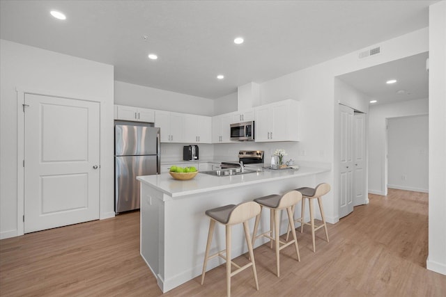 kitchen featuring a breakfast bar area, visible vents, a peninsula, stainless steel appliances, and white cabinetry