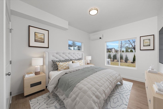 bedroom with baseboards, a wall unit AC, multiple windows, and wood finished floors