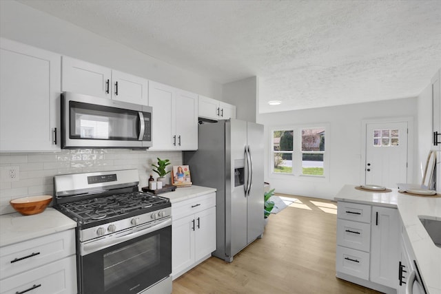 3903 E Hartson Ave, Spokane, WA 99202 - kitchen with appliances with stainless steel finishes, a textured ceiling, white cabinets, tasteful backsplash, and light wood-type flooring