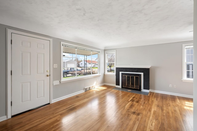 unfurnished living room with baseboards, visible vents, a fireplace with flush hearth, and wood finished floors