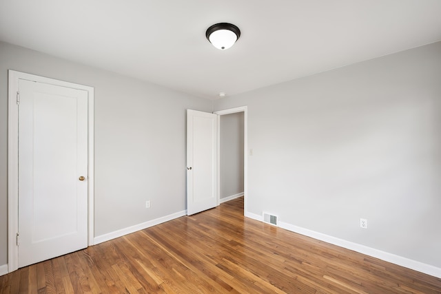 unfurnished bedroom with baseboards, wood finished floors, and visible vents