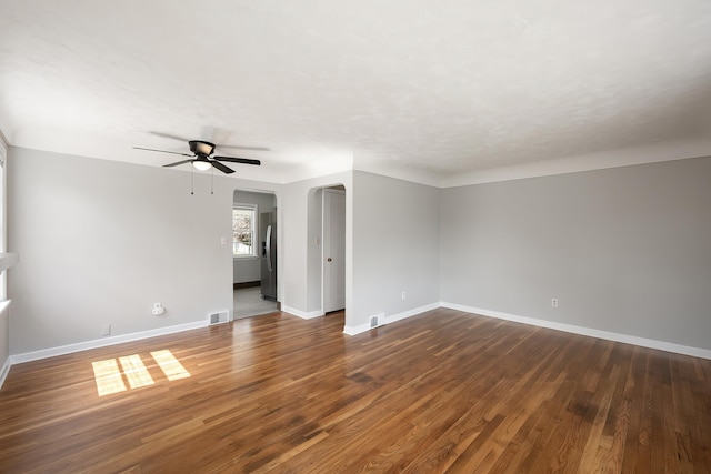unfurnished room with ceiling fan, dark wood-style flooring, visible vents, arched walkways, and baseboards