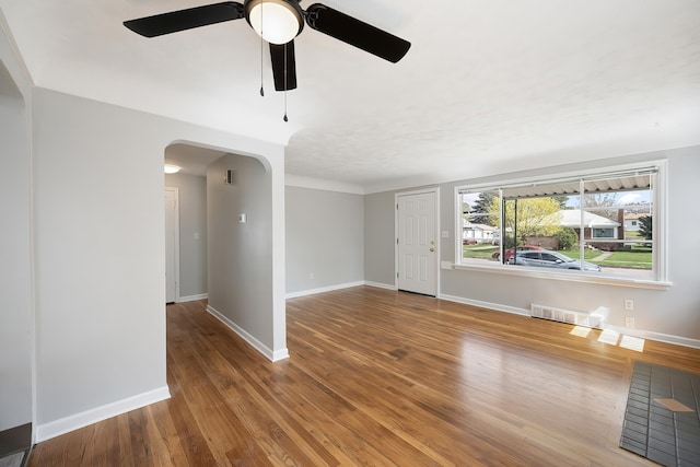unfurnished living room with arched walkways, ceiling fan, wood finished floors, and visible vents