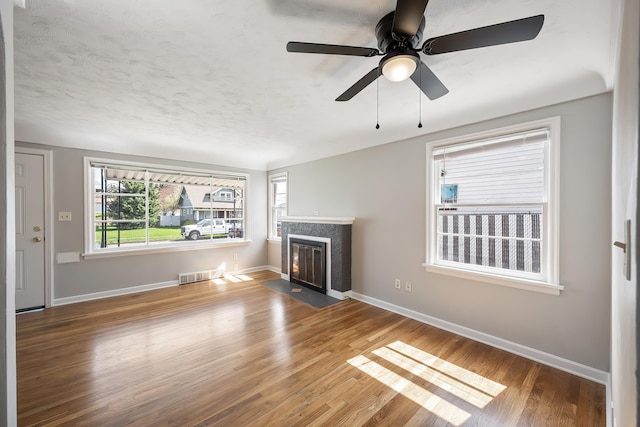 unfurnished living room with plenty of natural light, a premium fireplace, wood finished floors, and visible vents