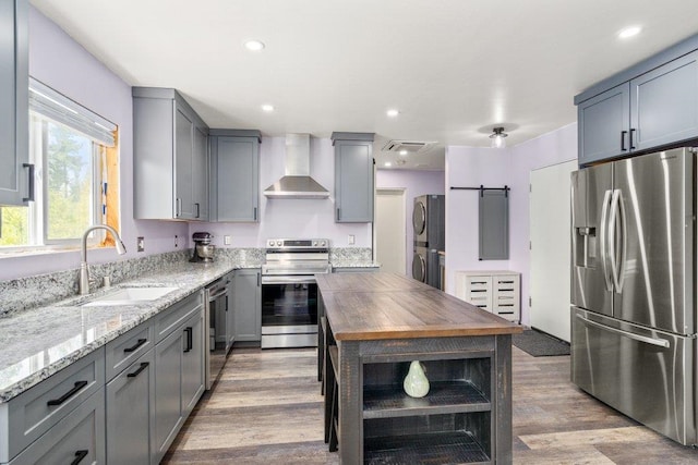 362 Panorama Dr, Newport, WA 99156 - kitchen with gray cabinets, appliances with stainless steel finishes, a sink, stacked washer and clothes dryer, and wall chimney exhaust hood