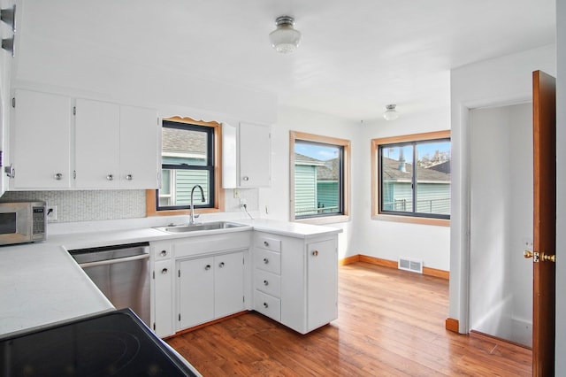 kitchen featuring appliances with stainless steel finishes, a sink, wood finished floors, backsplash, and visible vents