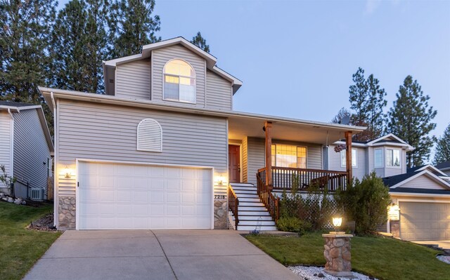 tri-level home featuring a front yard, stone siding, an attached garage, driveway, and a porch
