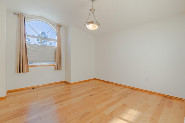 spare room featuring baseboards, vaulted ceiling, wood finished floors, and visible vents