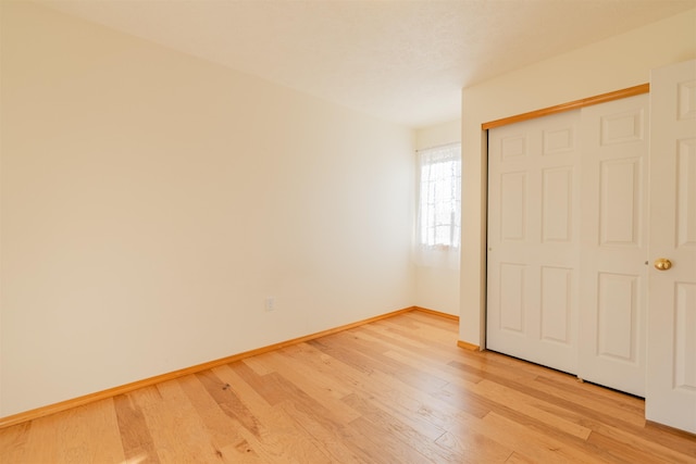 unfurnished bedroom featuring baseboards, a closet, and light wood-style flooring