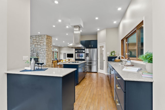kitchen with a kitchen island, blue cabinetry, island exhaust hood, appliances with stainless steel finishes, and a sink