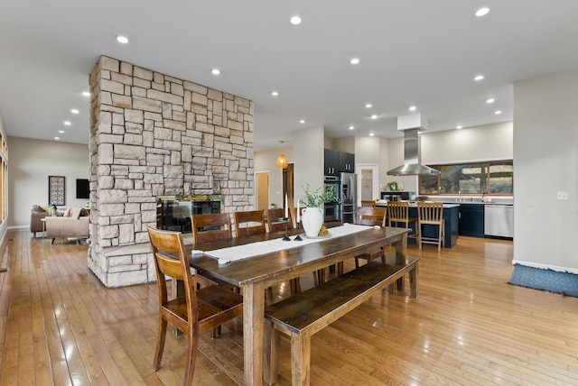 dining room with light wood-style floors, recessed lighting, baseboards, and a stone fireplace