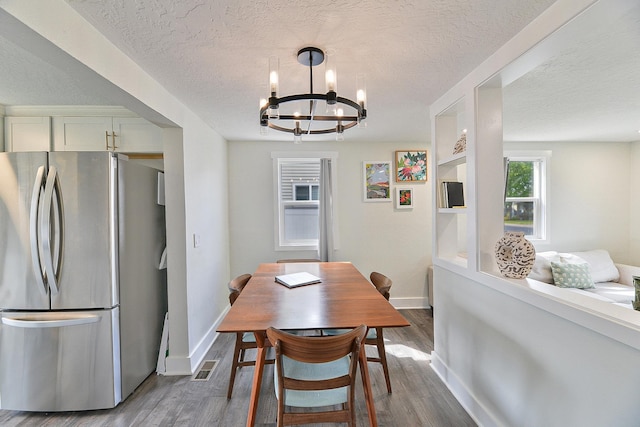 dining space with a textured ceiling, a notable chandelier, dark wood-style floors, and baseboards