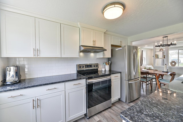 kitchen featuring dark stone counters, stainless steel appliances, light wood finished floors, and under cabinet range hood