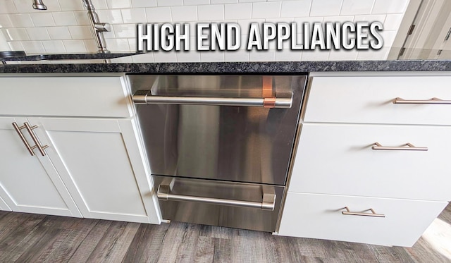 interior details featuring stainless steel dishwasher, dark wood finished floors, white cabinets, a sink, and dark stone countertops