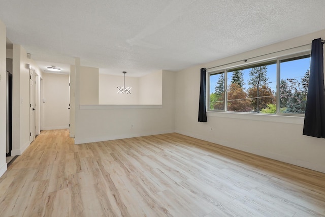 spare room featuring baseboards, light wood finished floors, a textured ceiling, and a chandelier