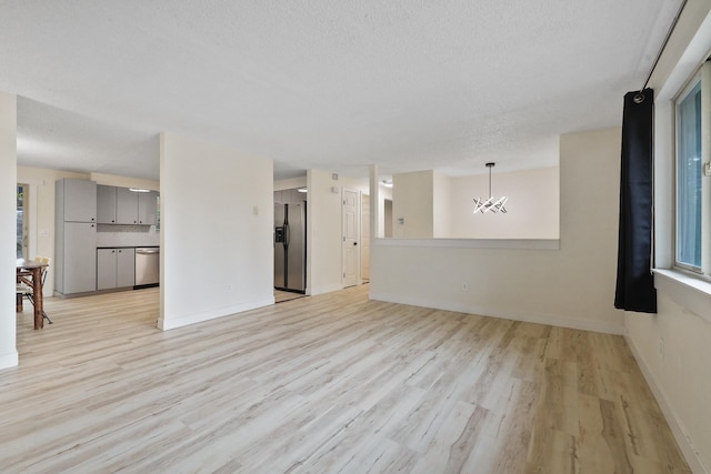 unfurnished living room featuring light wood-type flooring, a textured ceiling, baseboards, and an inviting chandelier