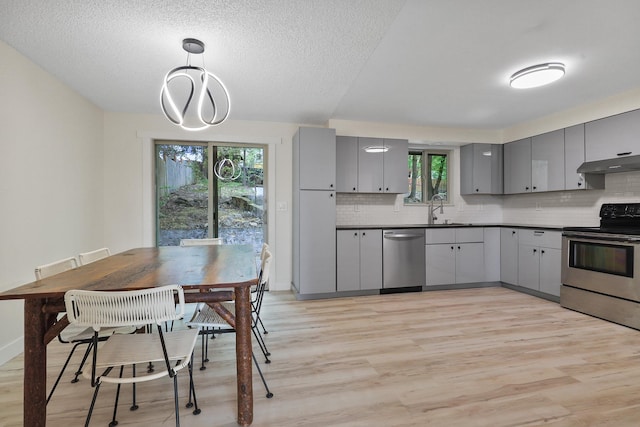 kitchen with appliances with stainless steel finishes, light wood-style floors, gray cabinets, a wealth of natural light, and under cabinet range hood